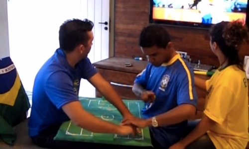 Hélio Fonseca Araújo e Regiane ajudaram o amigo Carlos (surdocego), a acompanhar o jogo de abertura do Brasil na Copa do Mundo